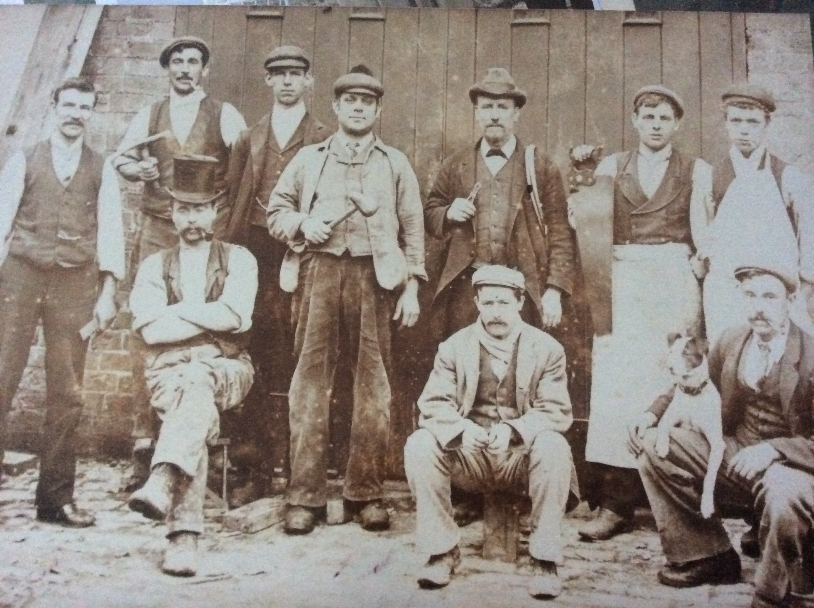 Group portrait of the Dalton masterbuilders, Wolverhampton, late 1800s. Thomas Dalton at back left with pipe and pickaxe; James Dalton bottom right with pipe and his dog Prince; William Dalton with large saw and carpenter's apron; Alexander Staveley Dalton far right.