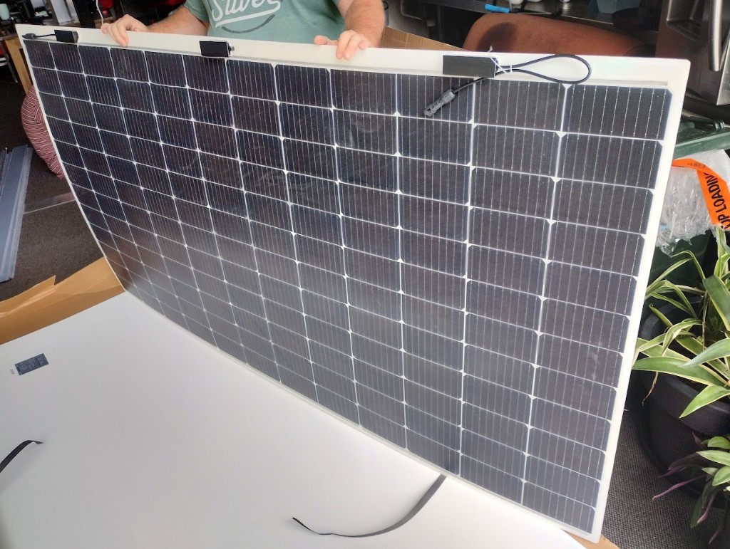 Flexible thin-film solar panel held up to show its bend and MC4 connector