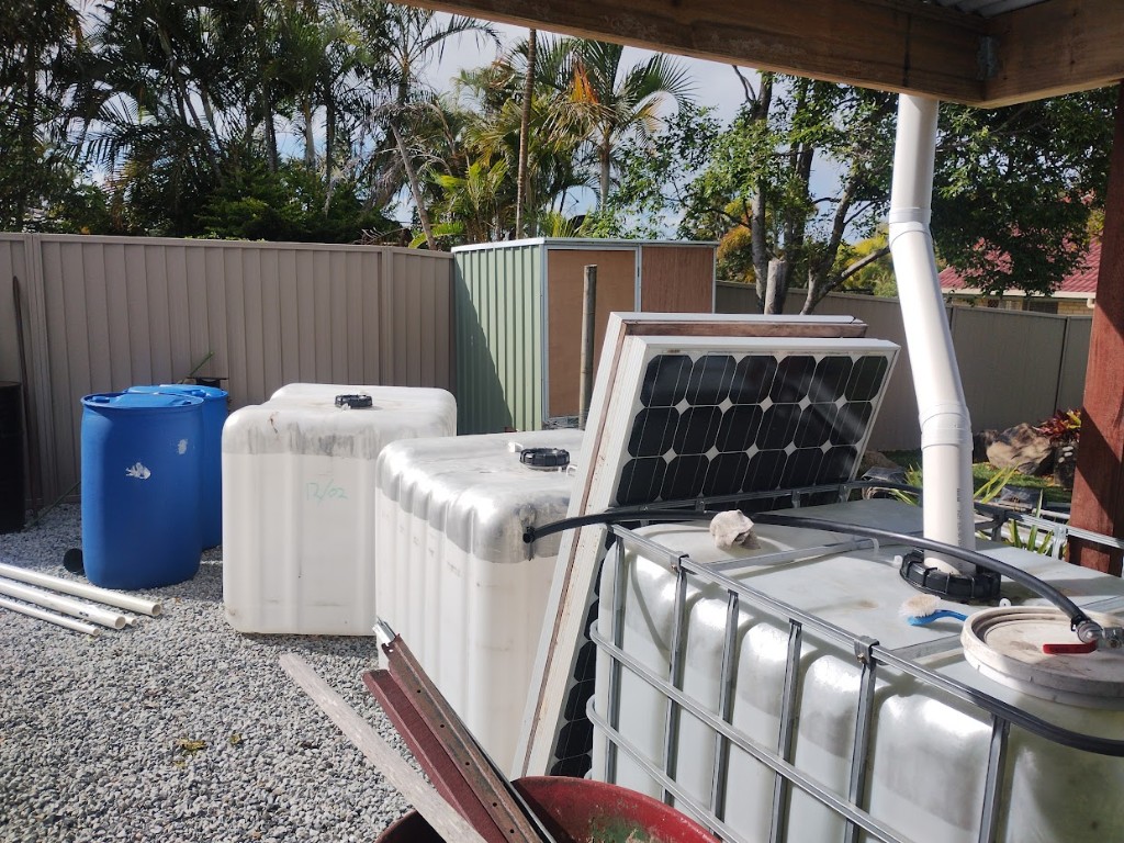 Salvaged solar panels beside IBC rainwater tanks in a backyard setup