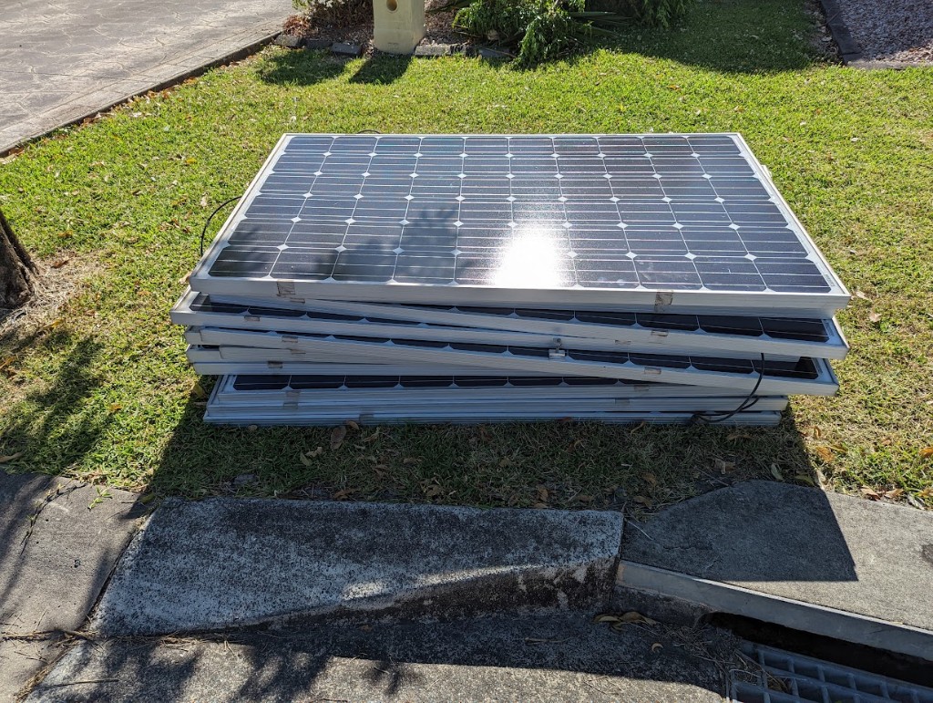 Stack of salvaged monocrystalline solar panels with MC4 cables on grass