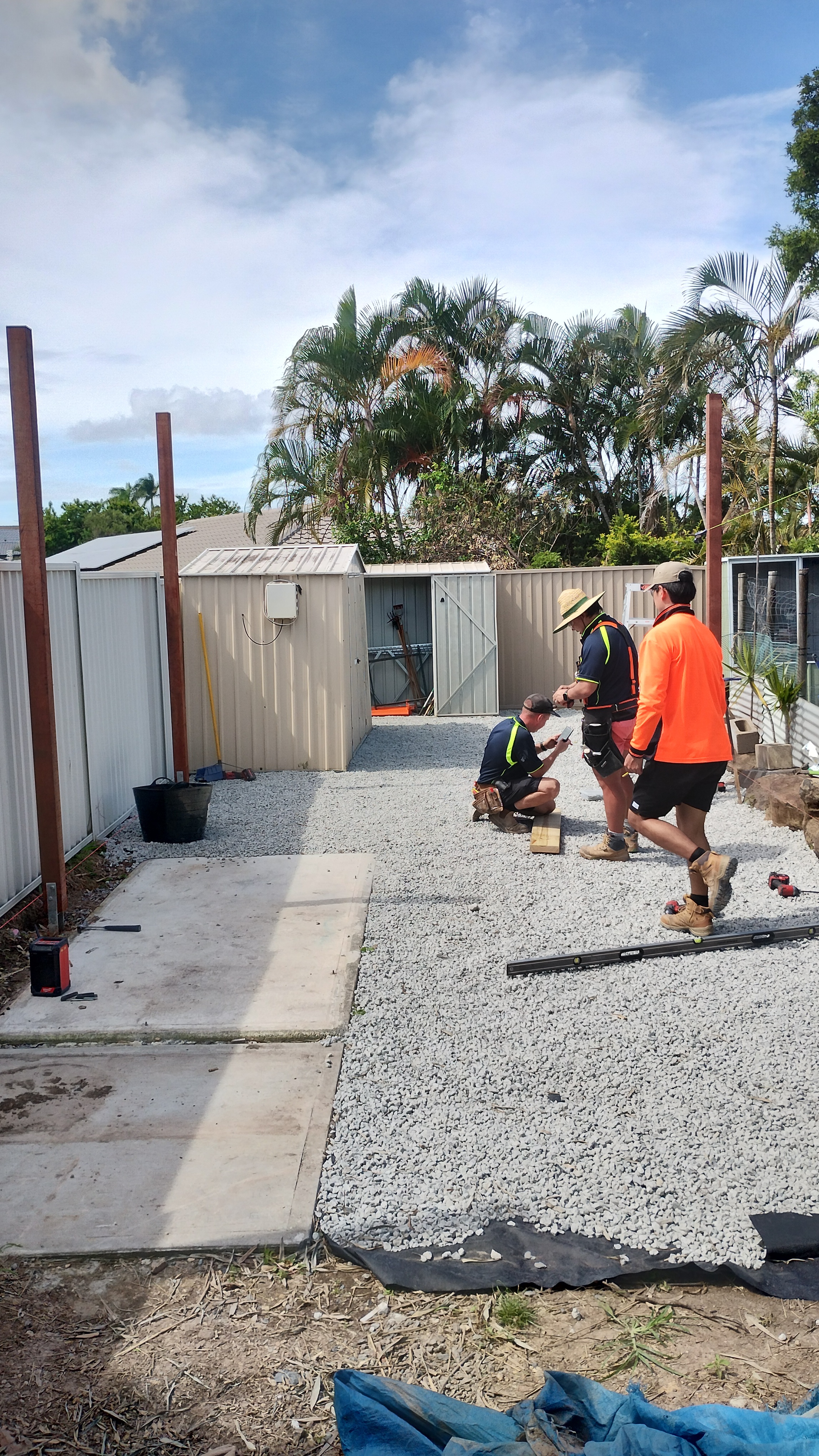 Two builders in hi-vis working on the shanty post and frame structure, with gravel and concrete pad visible