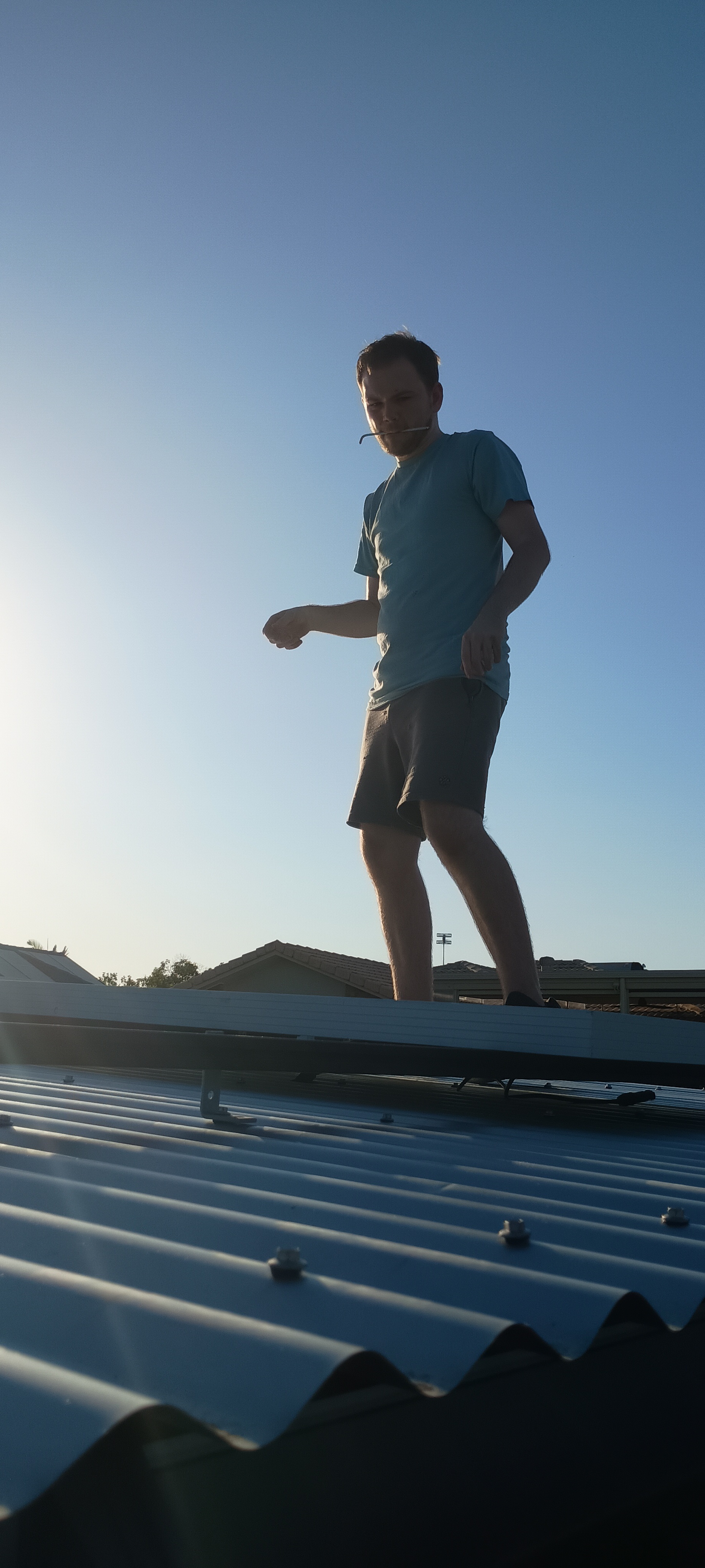 Young man helping mount salvaged solar panels on a corrugated steel shanty roof