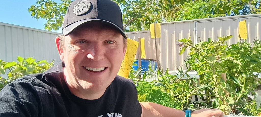 Steve Dalton smiling in the garden beside aquaponics beds, sticky traps, and leafy vegetables